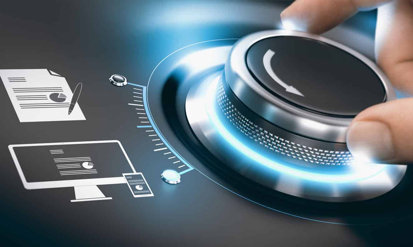 A person's hand is turning a large, glowing, metallic dial with a white arrow on it. To the left of the dial are several digital icons, including a document with a pen, a desktop monitor, a smartphone, and a tablet.